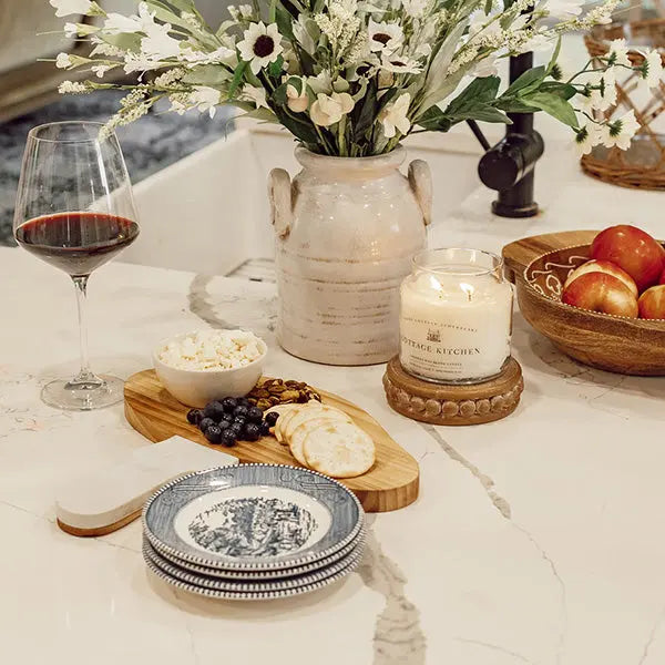 Marble and wood mushroom cutting board on a marble counter with cheese, crackers, blueberries, wine, and a candle.