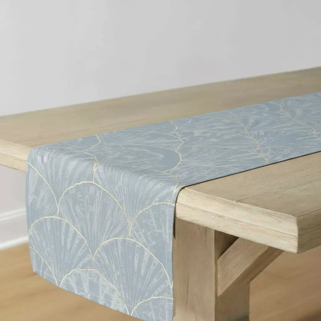 Blue Seashell Pattern Table Runner with shell illustrations on blue-gray background draped over a wooden table