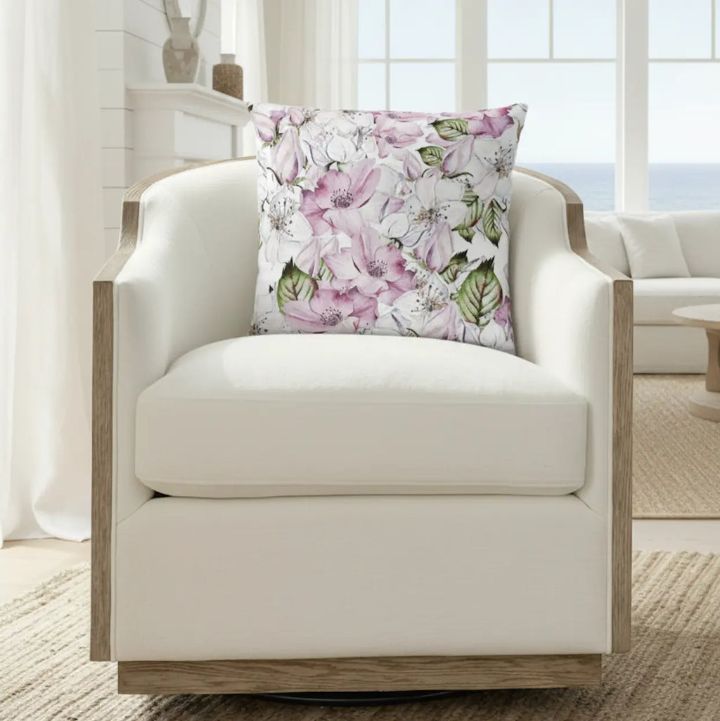 Pink and purple floral square throw pillow on a white armchair in a bright seaside living room.
