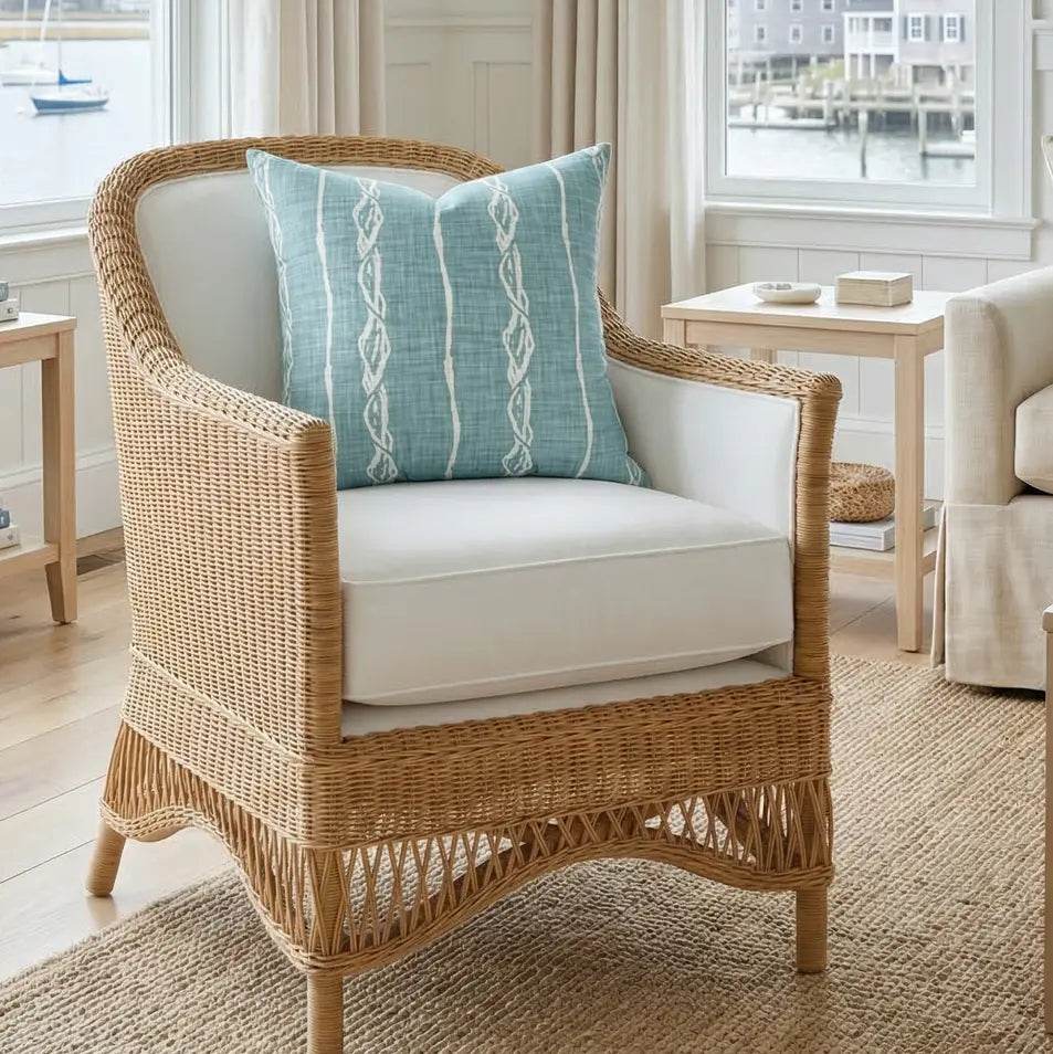 Marina Knot Throw Pillow in sea-glass teal rope-stripe, a coastal nautical accent on a woven wicker chair.