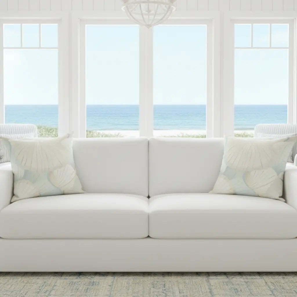 Seafoam Coastal Shells Throw Pillow with cream and pale blue-green shells on a white sofa.