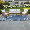 Outdoor patio set with wooden furniture and white cushions on a blue patterned rug.