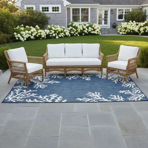 Outdoor patio set with wooden furniture and white cushions on a blue patterned rug.