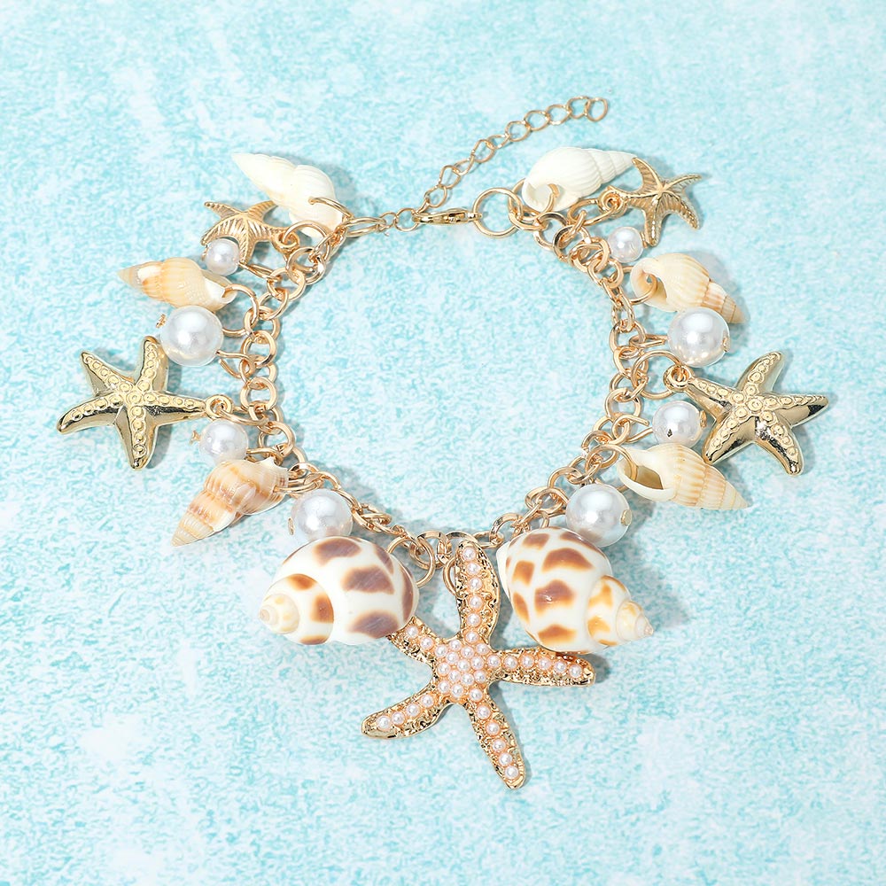Coastal shell starfish pearl charm station bracelet styled as beach inspired jewelry on a wrist.