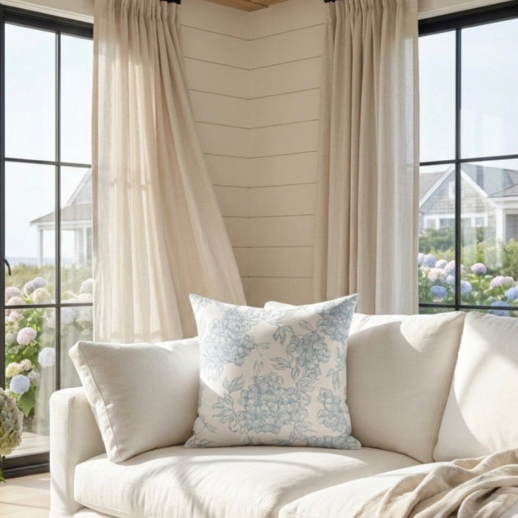 Blue and white floral pillow on a sofa with light neutral textiles in a modern coastal home.