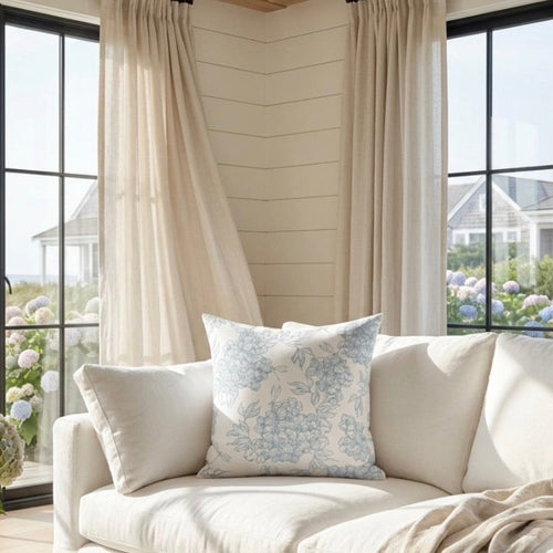Blue and white floral pillow on a sofa with light neutral textiles in a modern coastal home.