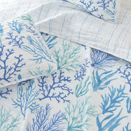 Blue coral pattern quilt styled on a wood bed frame in an ocean-inspired bedroom