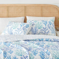 Blue coral quilt on a bed with white sheets in a coastal beach house bedroom.