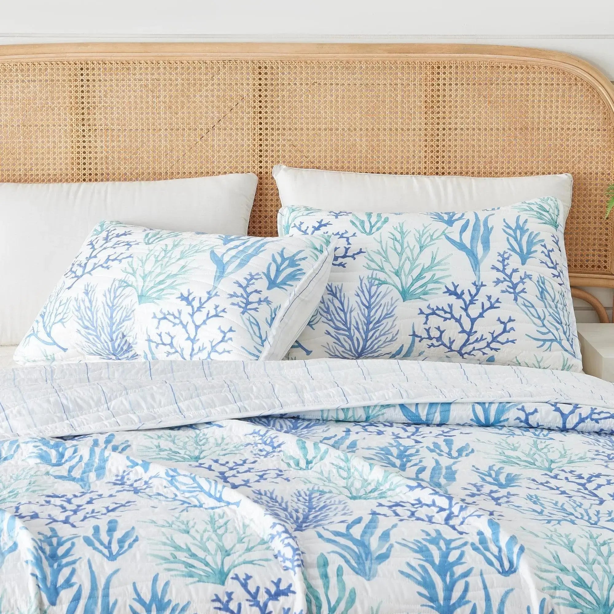 Blue coral quilt on a bed with white sheets in a coastal beach house bedroom.