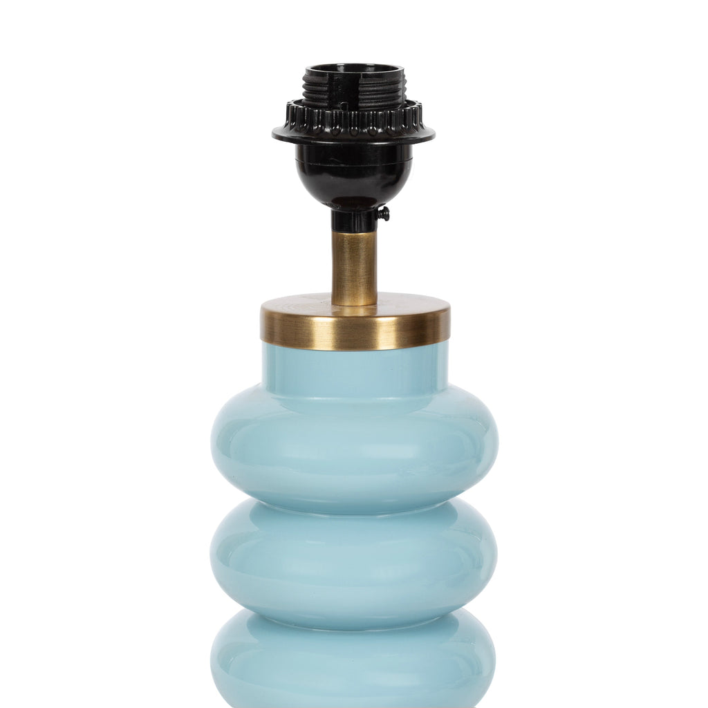 Blue ceramic lamp with warm brass trim, styled beside a woven tray in a bright coastal living room.
