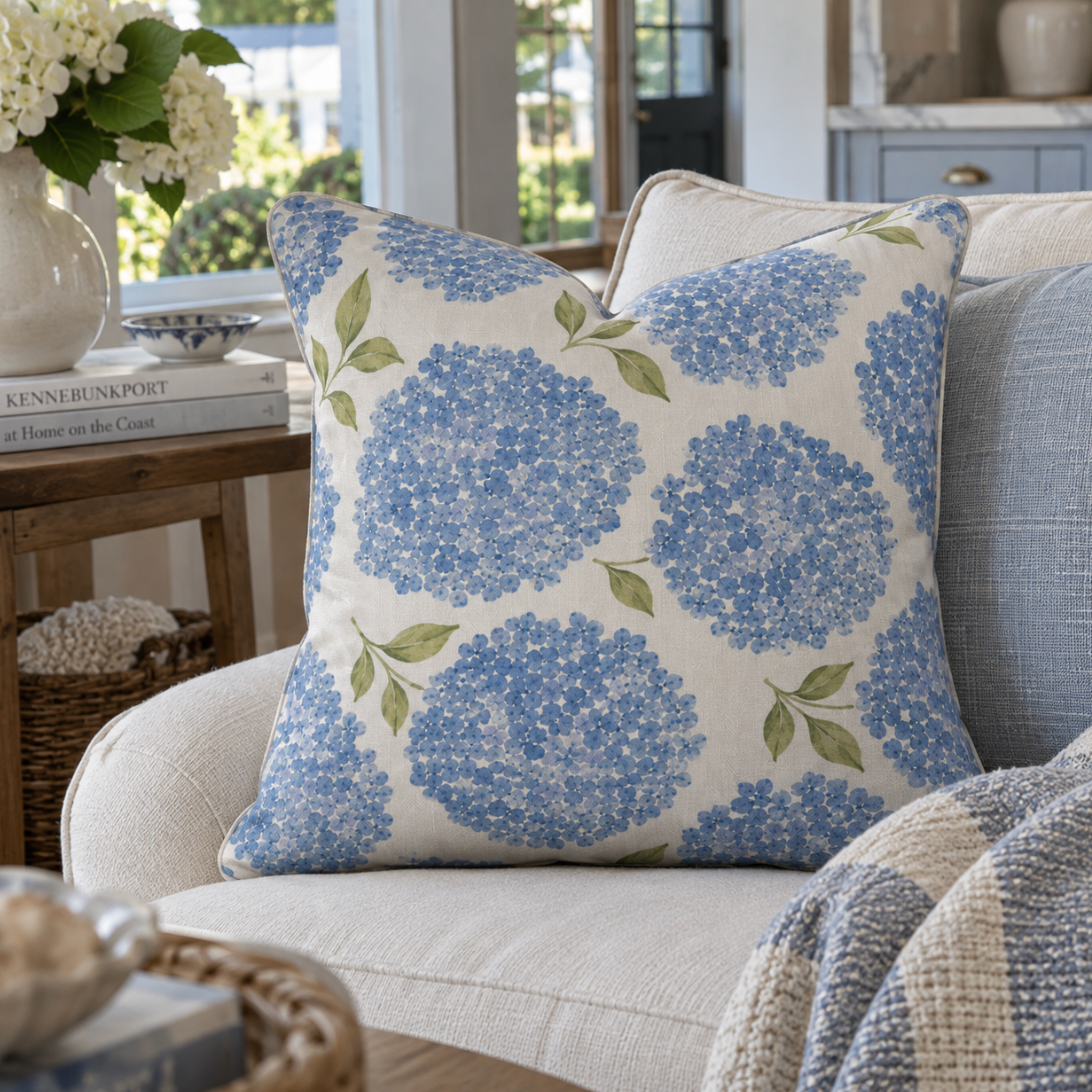 Blue hydrangea coastal throw pillow with watercolor flower clusters and green leaves on an ivory background