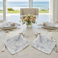 Blue paisley floral cloth napkins set of four with gold napkin rings on a marble table by seaside window.