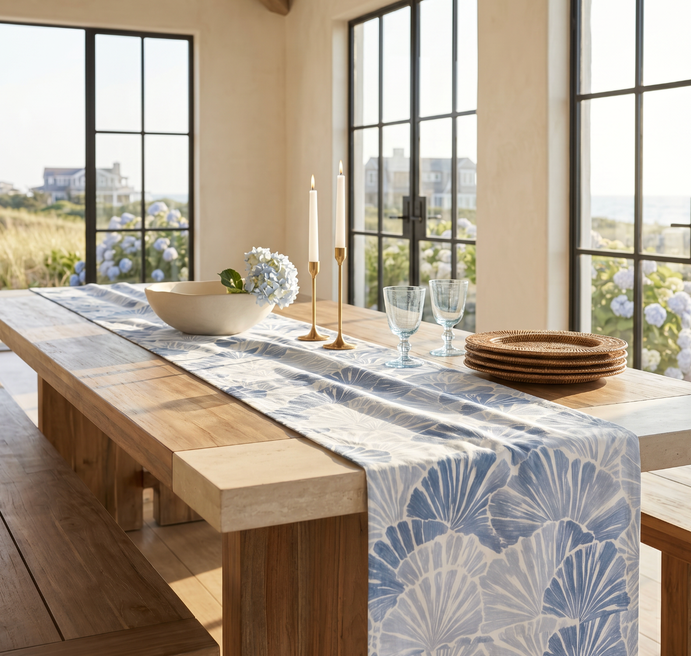 Blue and white coastal table runner with shell design on a long wood table set with woven chargers and linen napkins.