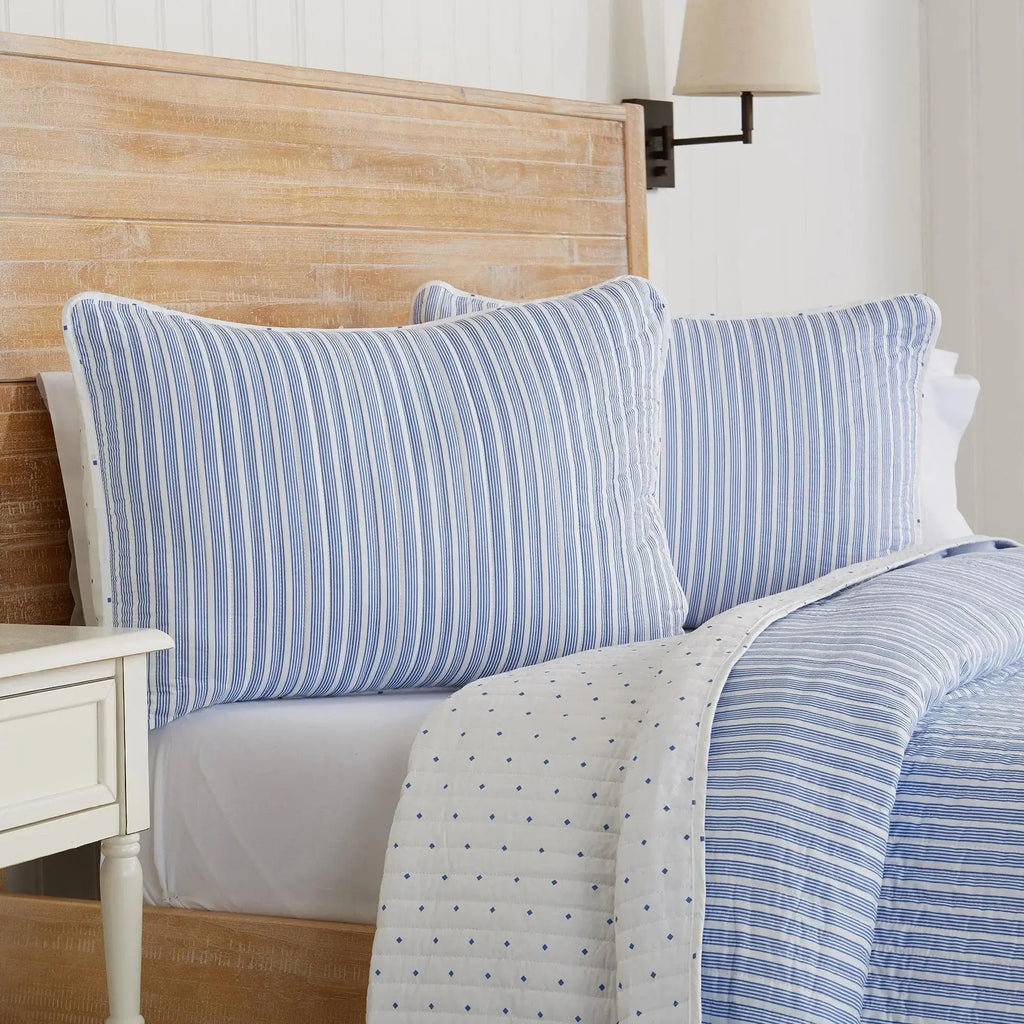 Blue striped quilt set styled with white pillows in a light and airy coastal bedroom.