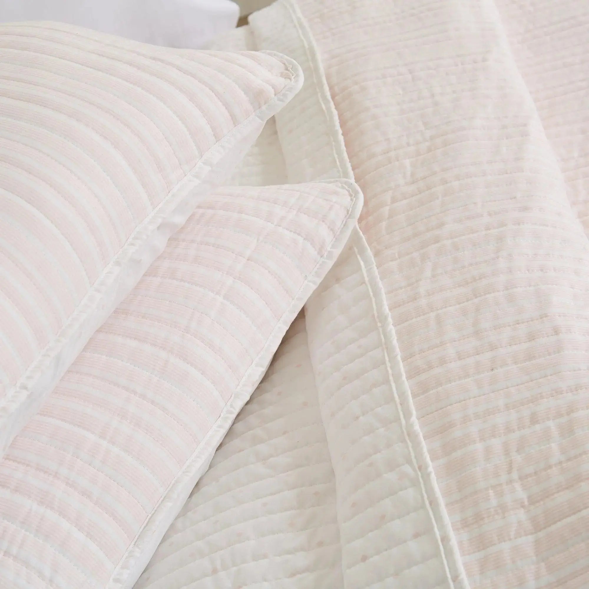 Blush pink striped quilt and shams creating light, feminine bedding in a beach cottage bedroom