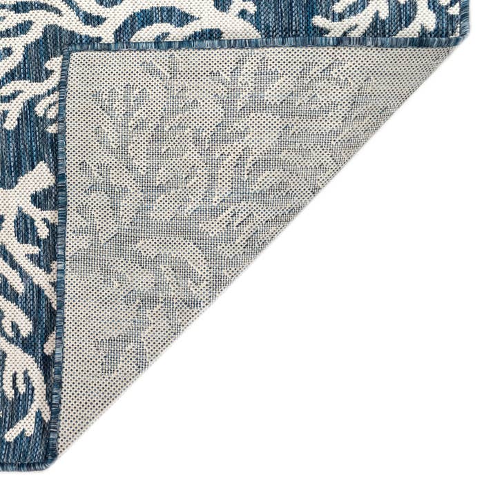 Corner of a blue and white coral patterned rug on a white background