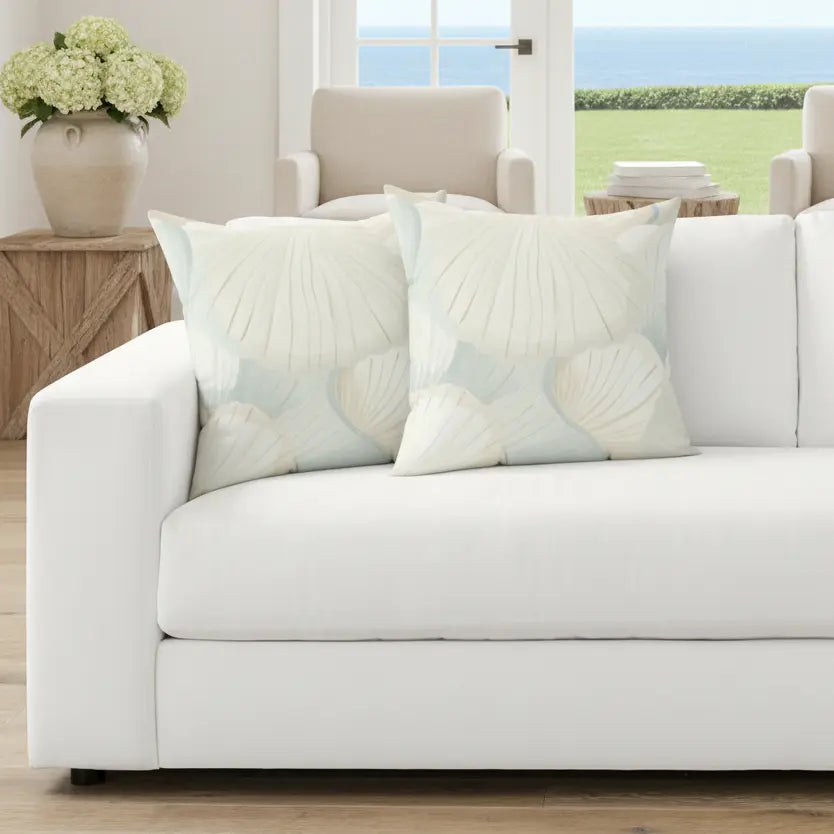 Seafoam Coastal Shells Throw Pillow with cream and pale blue-green shell patterns on a white sofa