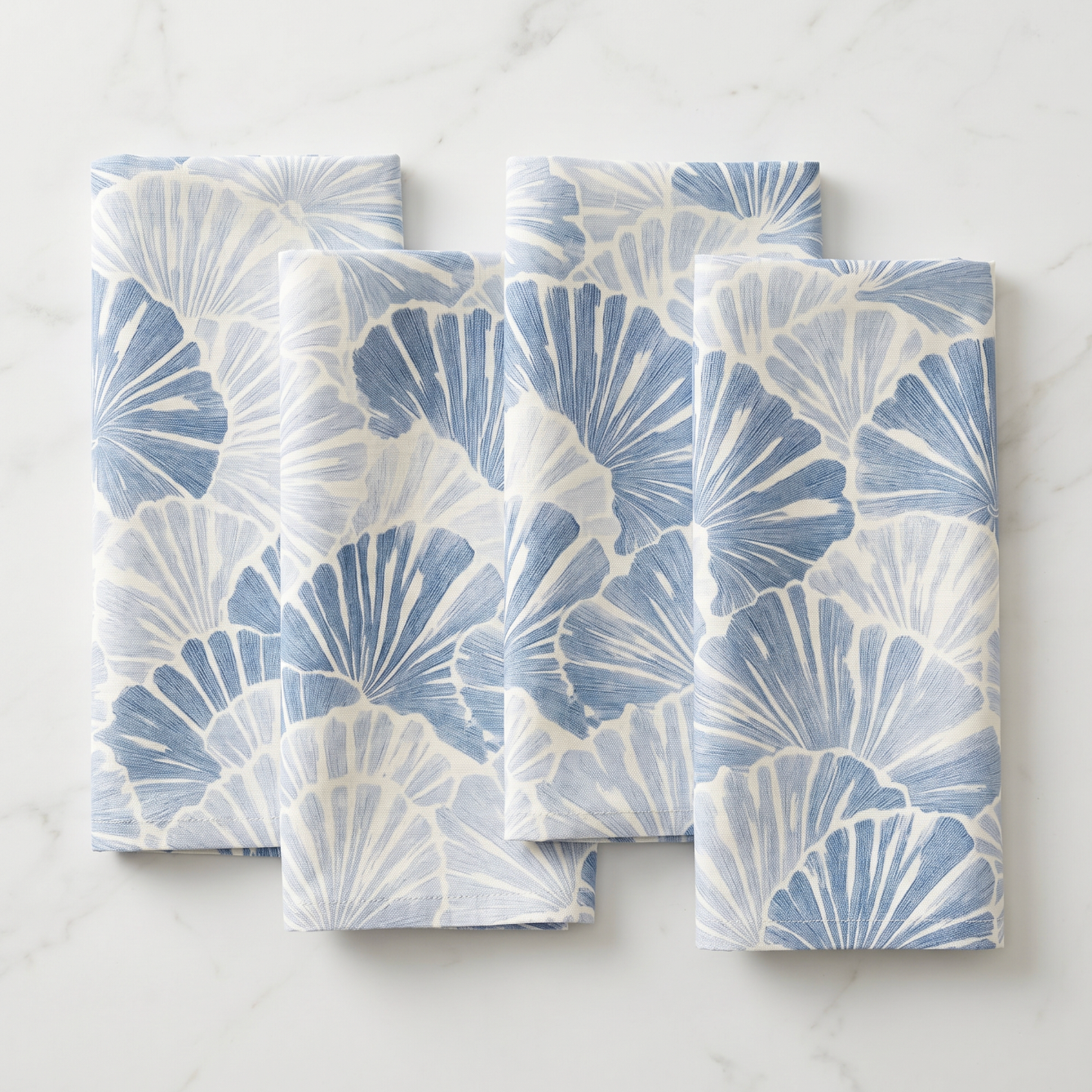 Stack of four blue shell fan pattern linen napkins arranged on a wooden farmhouse table for summer entertaining