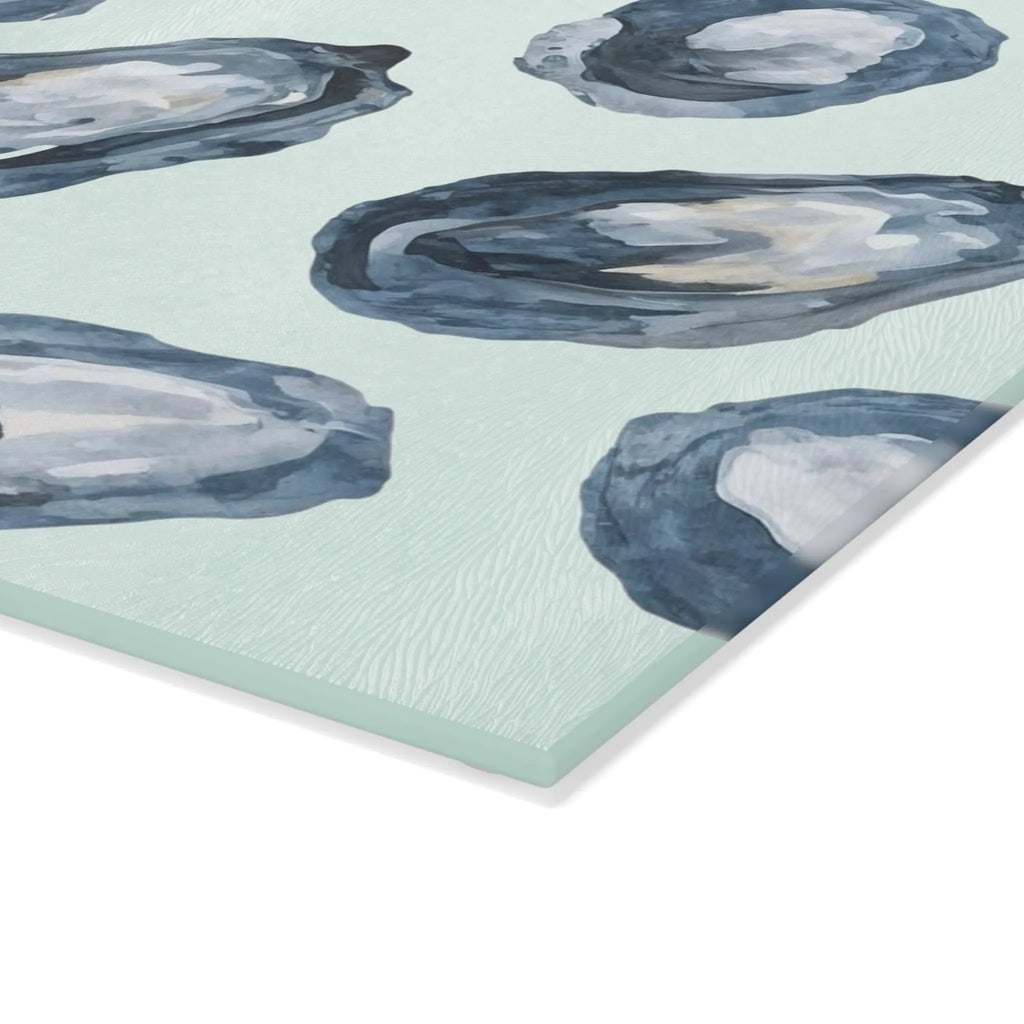 Oyster-pattern tempered glass cutting and serving board with blue oyster motifs on a pale sea-green surface.