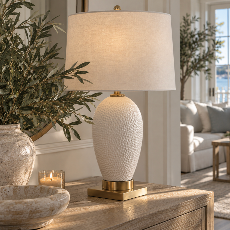 Coastal table lamp with dimpled white ceramic body, brass hardware, and neutral linen shade for living room or bedroom decor