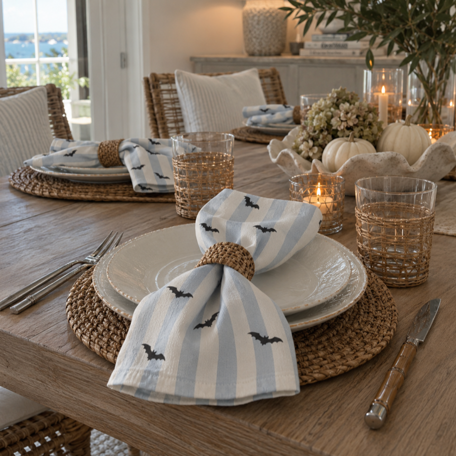 Set of 4 blue and white striped linen napkins with black bat print, folded in woven rattan napkin rings for a coastal Halloween table setting