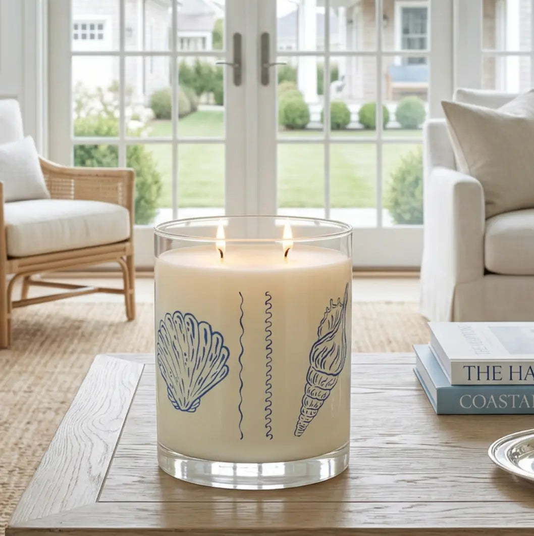 Seashell Reverie Ocean Mist Candle by Printify; blue seashell sketch designs on a clear glass jar atop a wooden table.