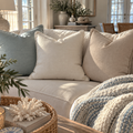 Seafoam blue, ivory, and oatmeal linen-look throw pillows with pom pom trim layered on a cream coastal sofa