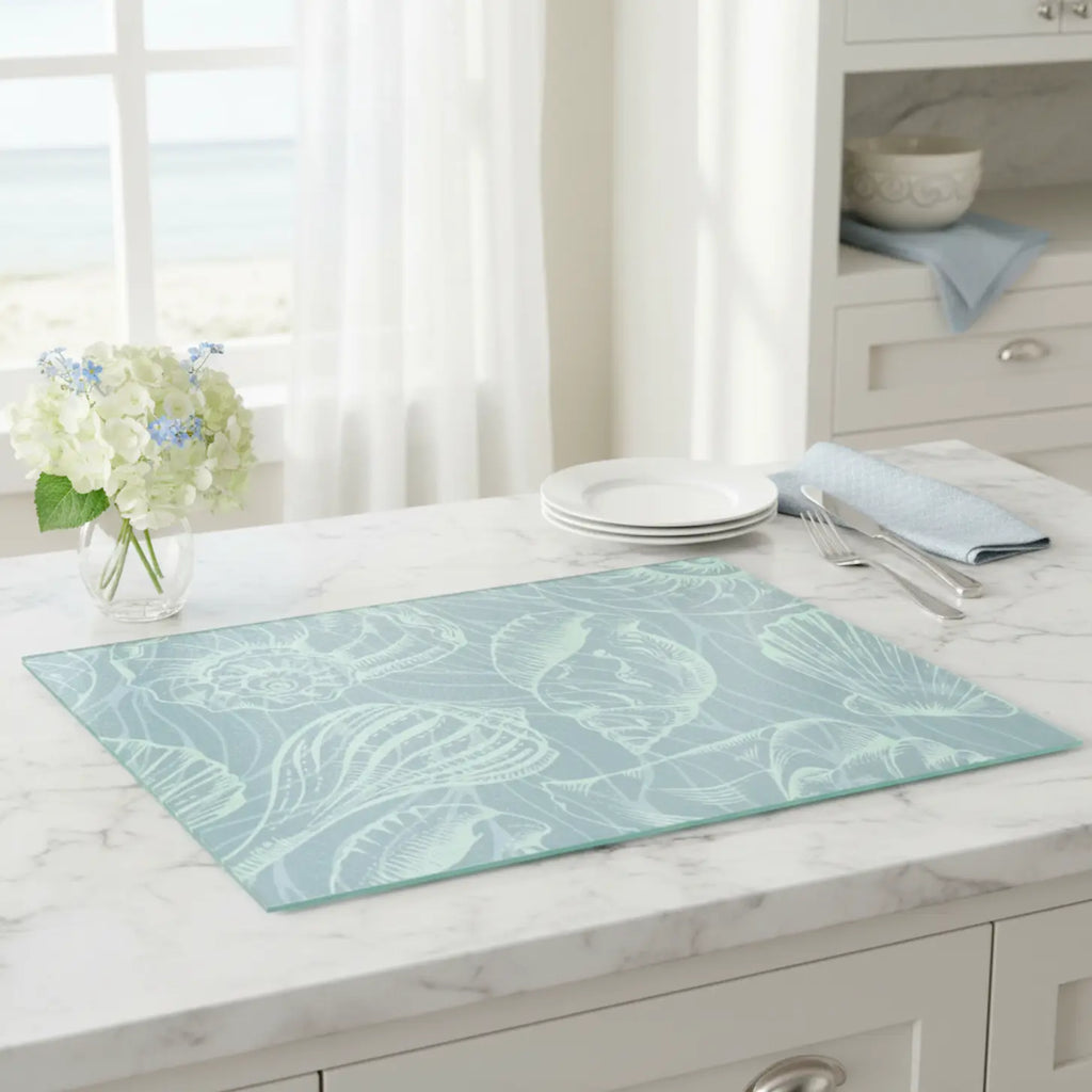 Coastal Seashell Glass Cutting Board in seafoam tempered glass with shell motif on marble countertop.