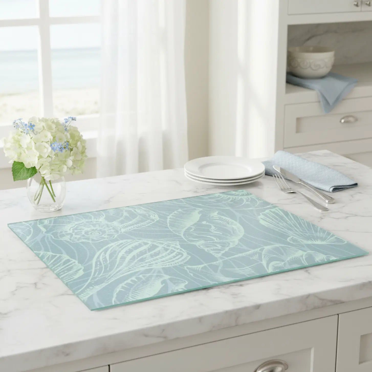 Coastal Seashell Glass Cutting Board in seafoam tempered glass with shell motif on marble countertop.