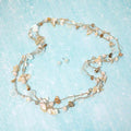 Shell natural stone and pearl charm station coastal layered long necklace shown as beach inspired statement jewelry.