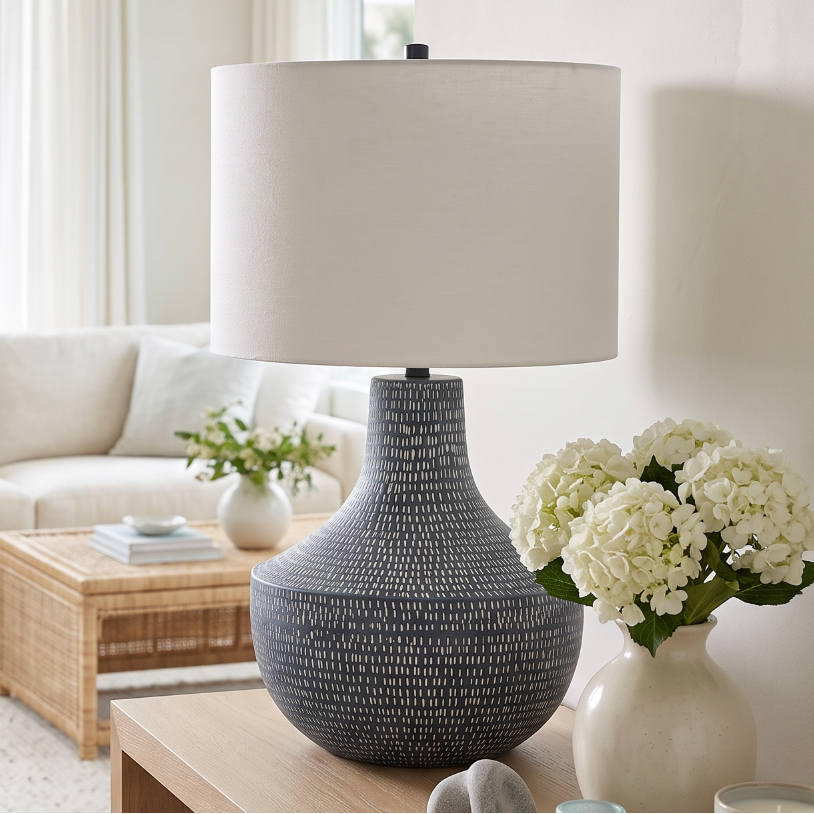 Textured blue gray ceramic lamp with a rounded bottle‑shape base, styled on a light wood console.