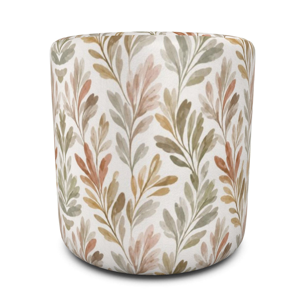 Round upholstered ottoman with repeating leafy sprigs in muted green, tan, and blush on a cream background.