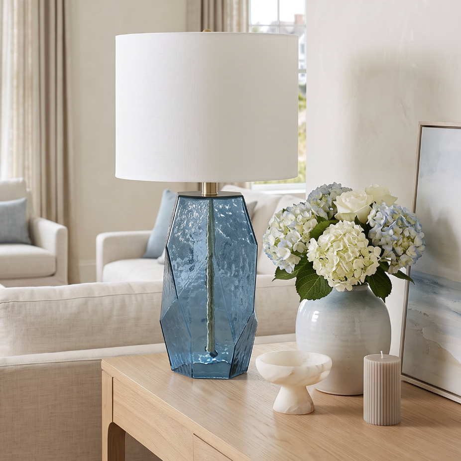 Faceted aqua blue glass table lamp with an angular geometric base and a large white drum shade.