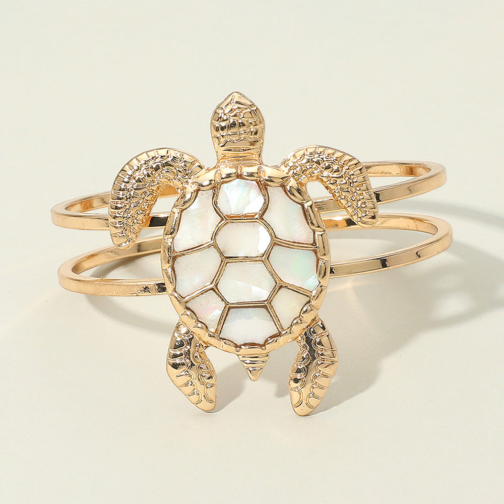 Gold turtle hinged bracelet featuring a mother of pearl shell detail worn in a beach inspired outfit.
