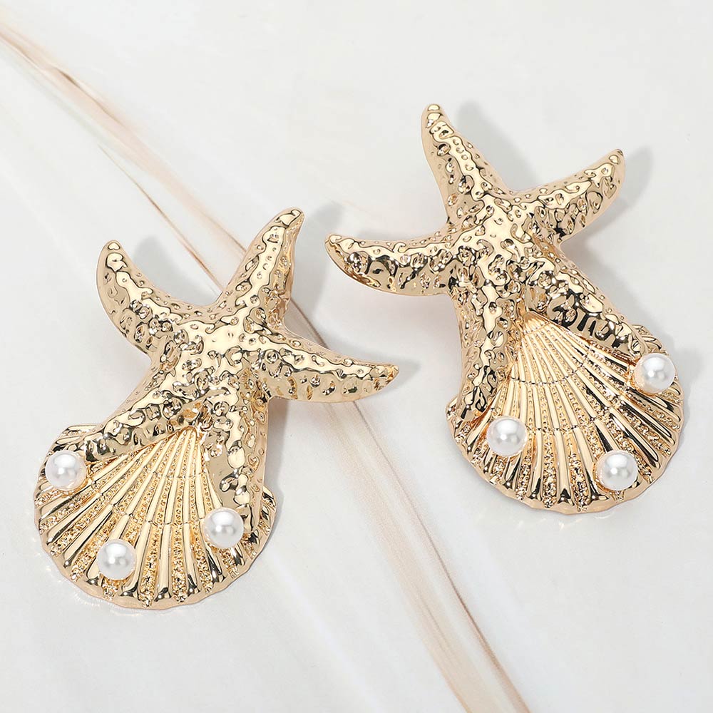 Gold Textured starfish shell earrings with pearl accent shown as beach inspired statement jewelry