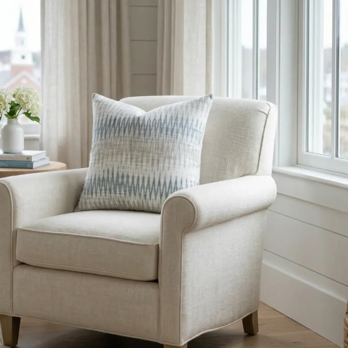 Stonewash Ikat Throw Pillow on a beige armchair by a sunlit window, blue and neutral ikat pattern.