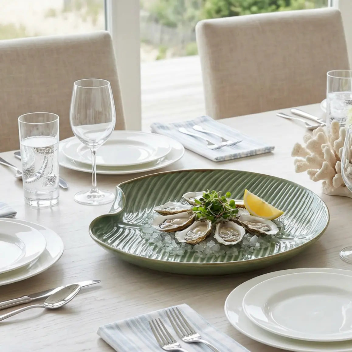 Dining table set with a green plate of oysters, glasses, and cutlery.