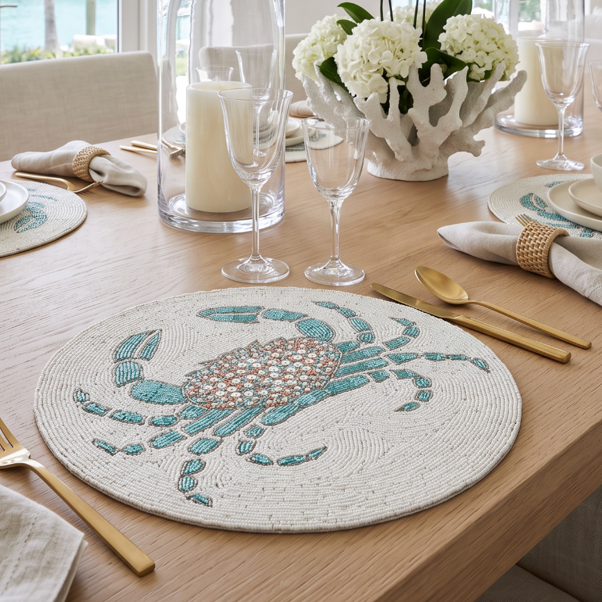 Cream and aqua hand‑beaded crab placemat creating a playful seaside accent at each place setting.