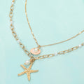 Layered gold seashell starfish necklace shown as beach inspired everyday jewelry.