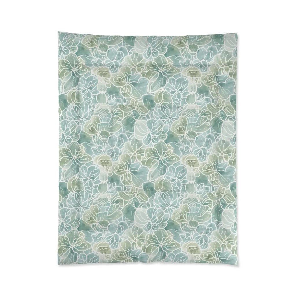 Light blue/green floral comforter layered with white pillows and a throw in a beach house guest room.