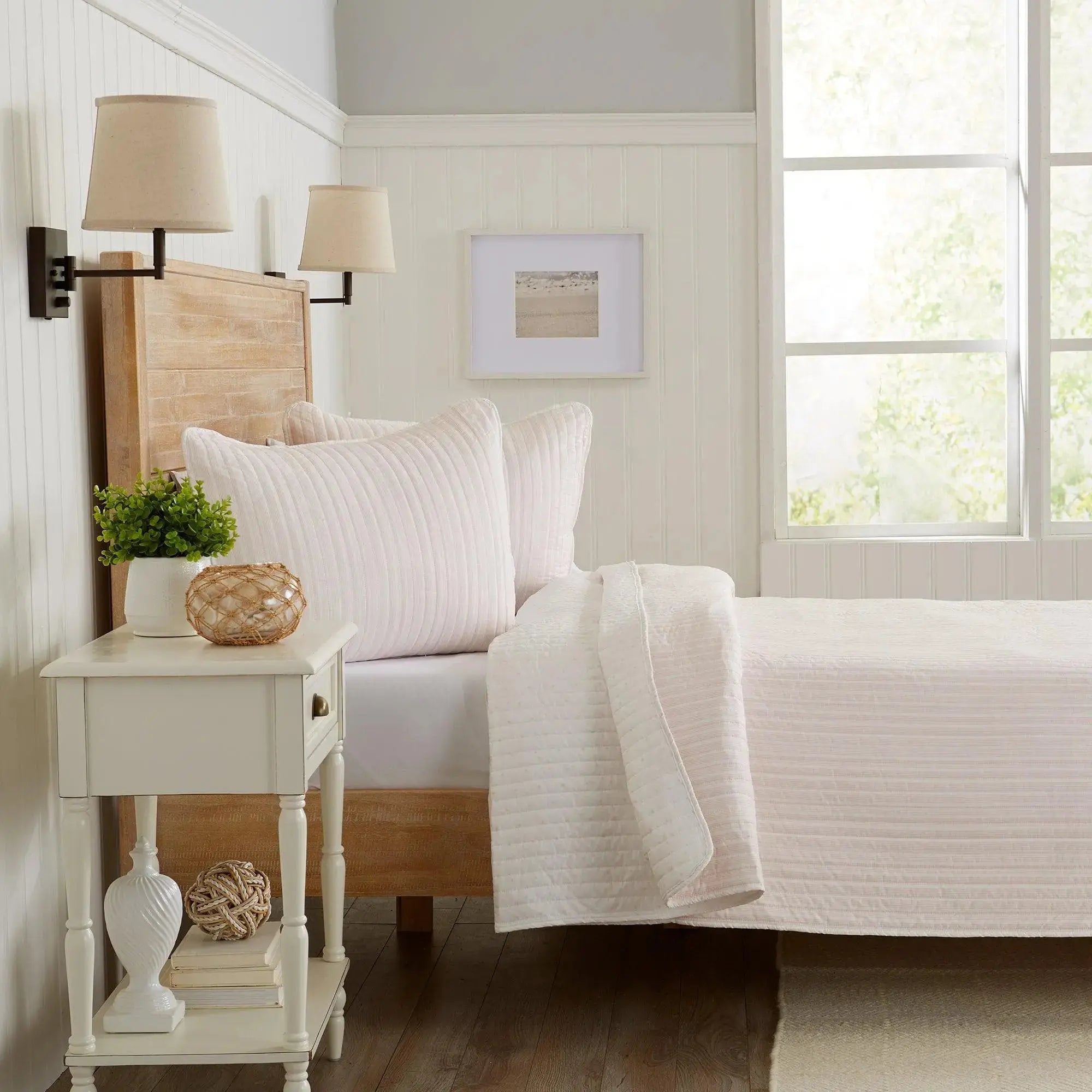 Light pink stripe quilt 3-piece set on a queen bed in a bright coastal room
