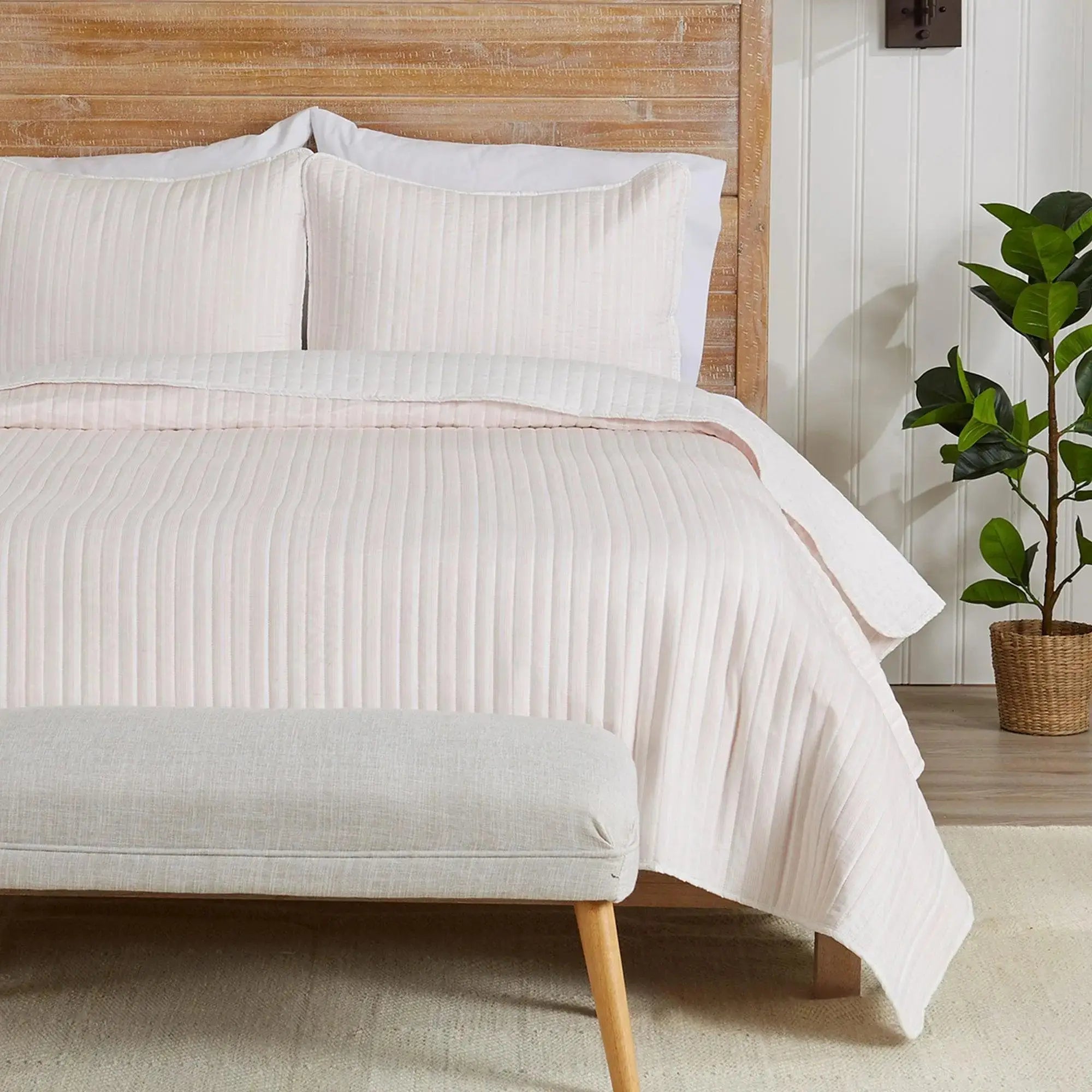Light pink 3-piece stripe quilt set on a bed with white sheets in a soft coastal bedroom