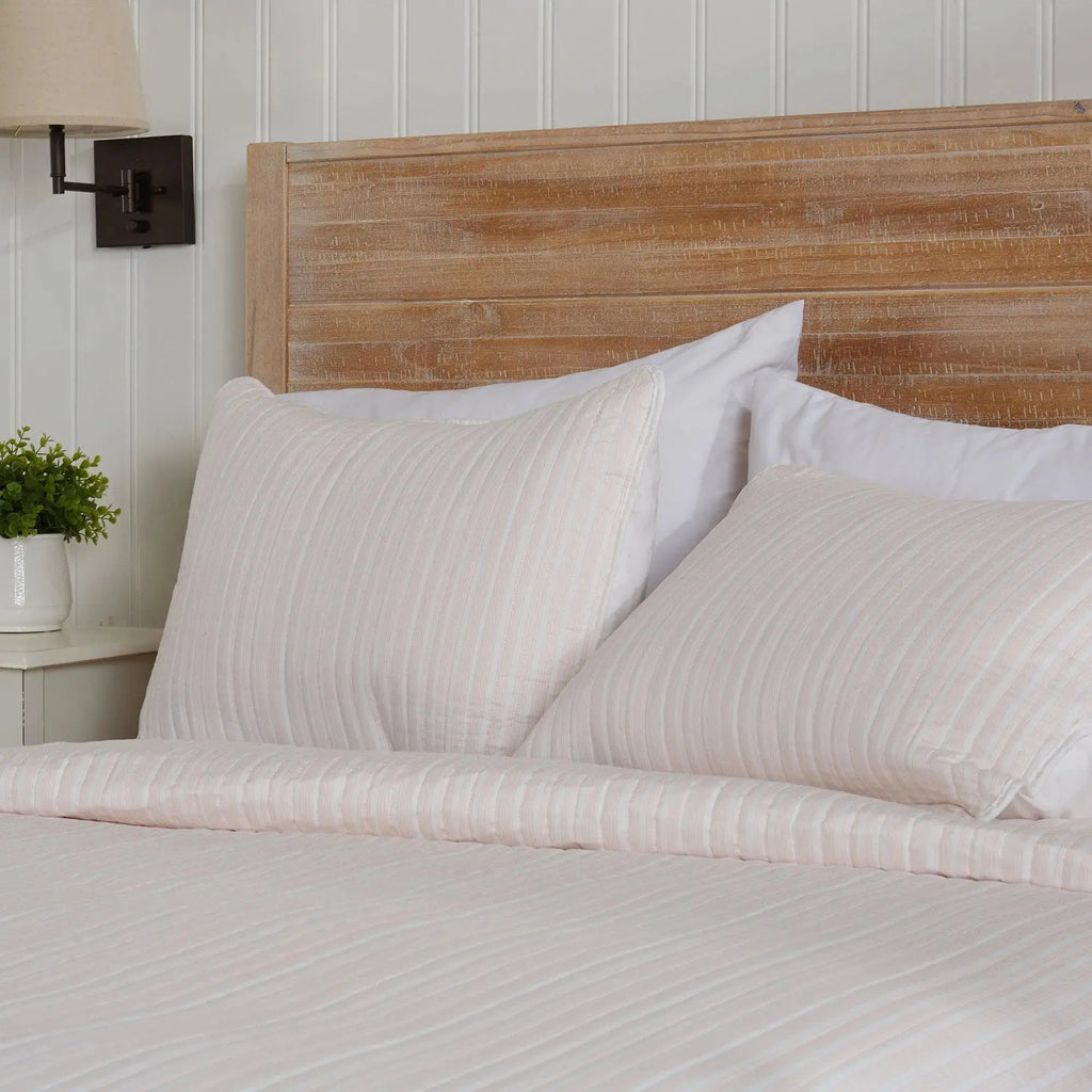 Light pink striped quilt set styled with white pillows in a cozy seaside guest room.