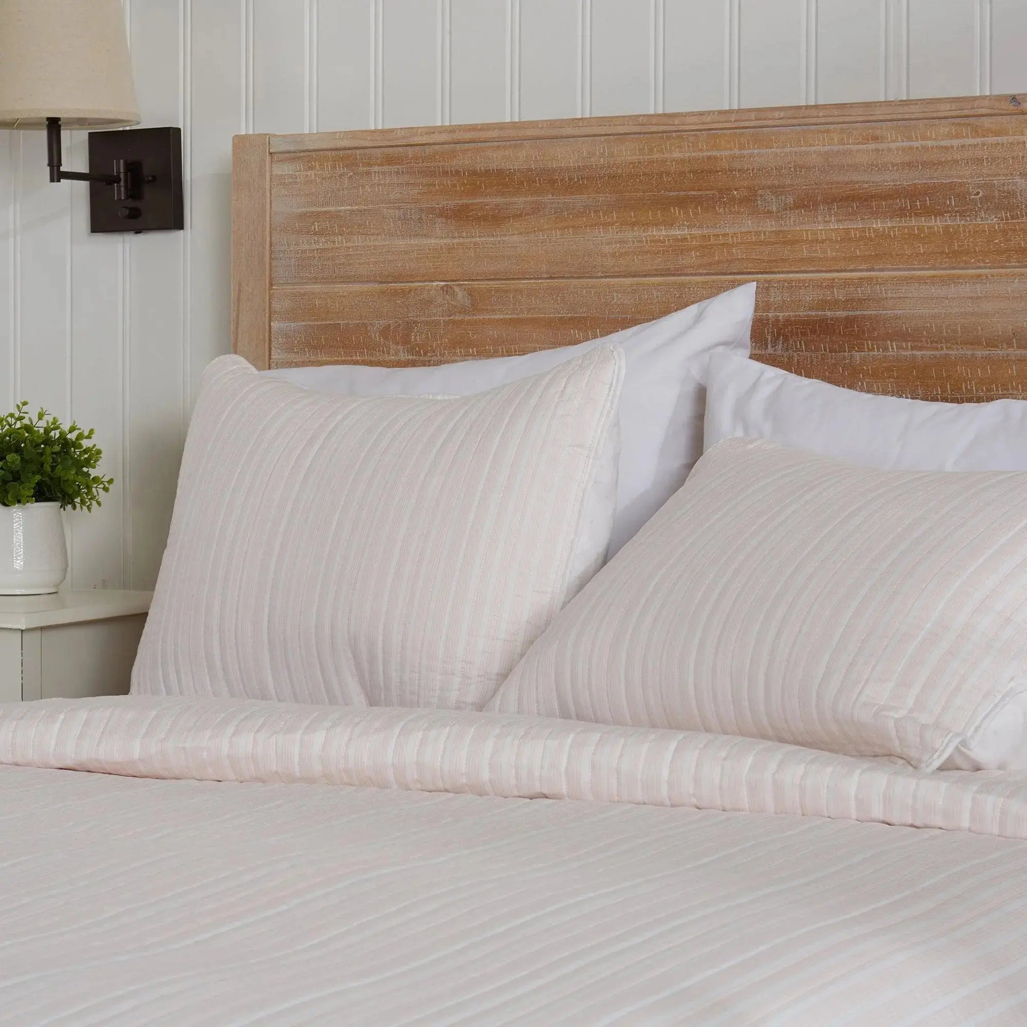 Light pink striped quilt set styled with white pillows in a cozy seaside guest room.