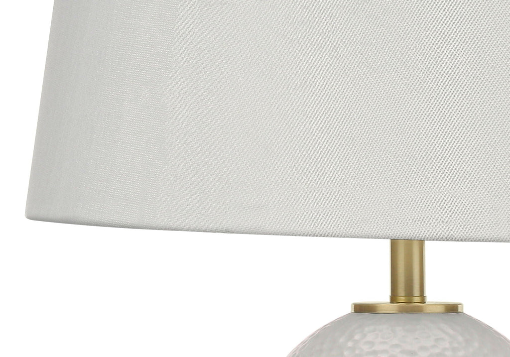 Hand-textured white ceramic table lamp with dimpled surface and warm brass base, adding organic texture to a neutral living room