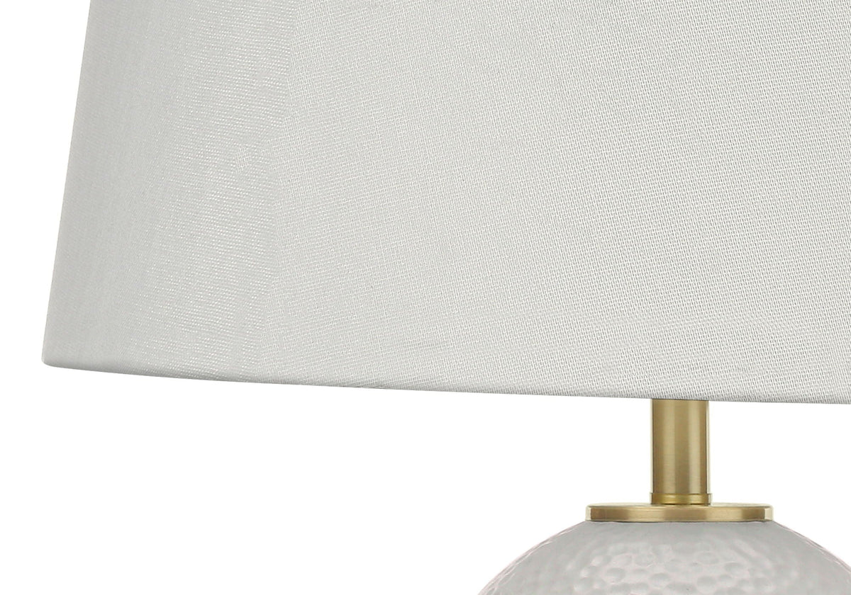 Hand-textured white ceramic table lamp with dimpled surface and warm brass base, adding organic texture to a neutral living room