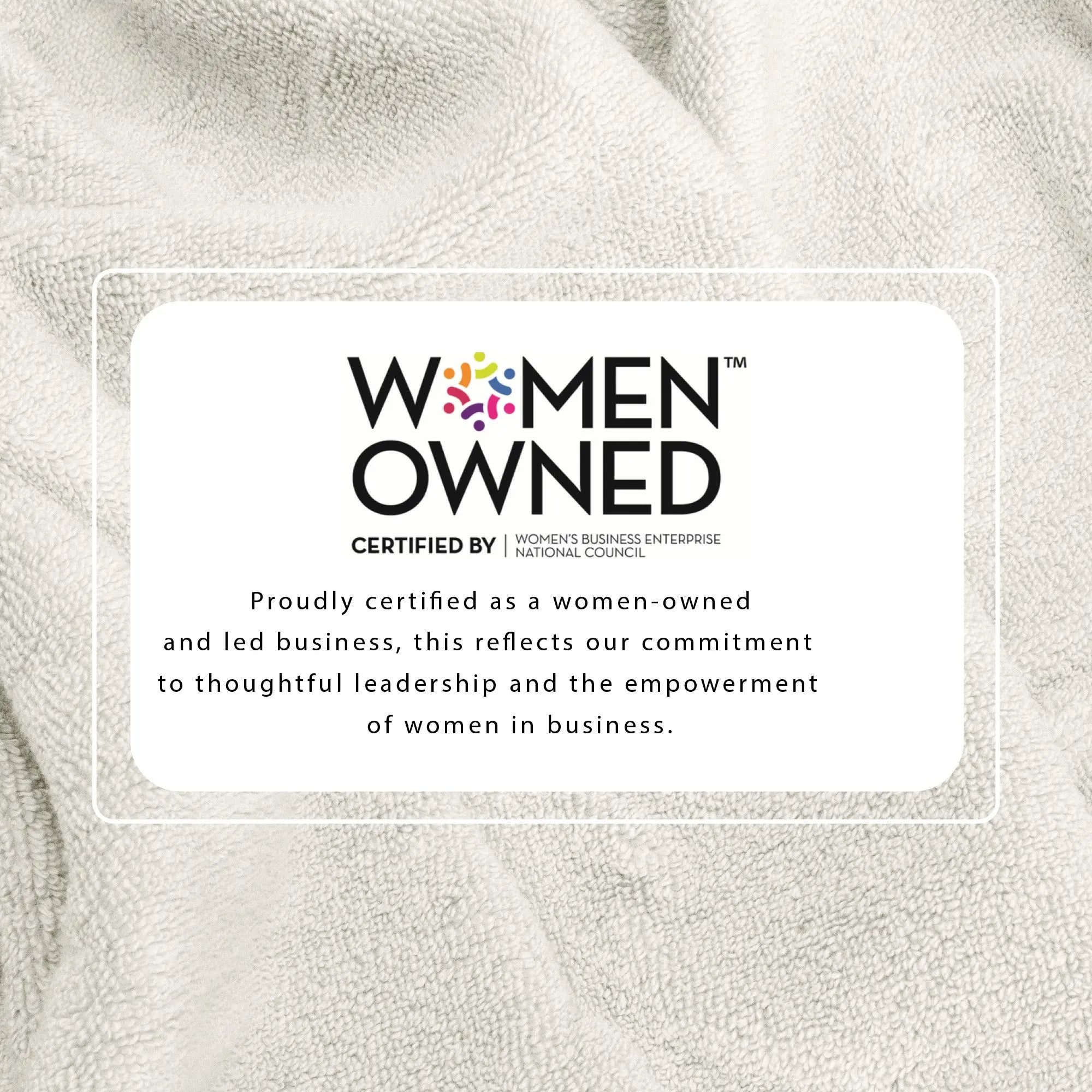 100% cotton bath towel with Women-Owned certification badge on beige fabric.