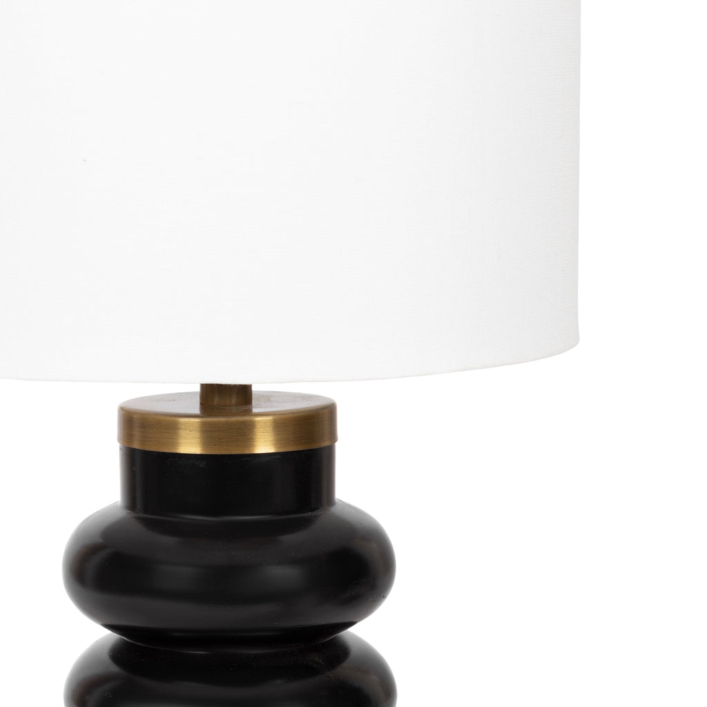 Black accent lamp with a sculptural stacked base, styled on a console table in a neutral living room.