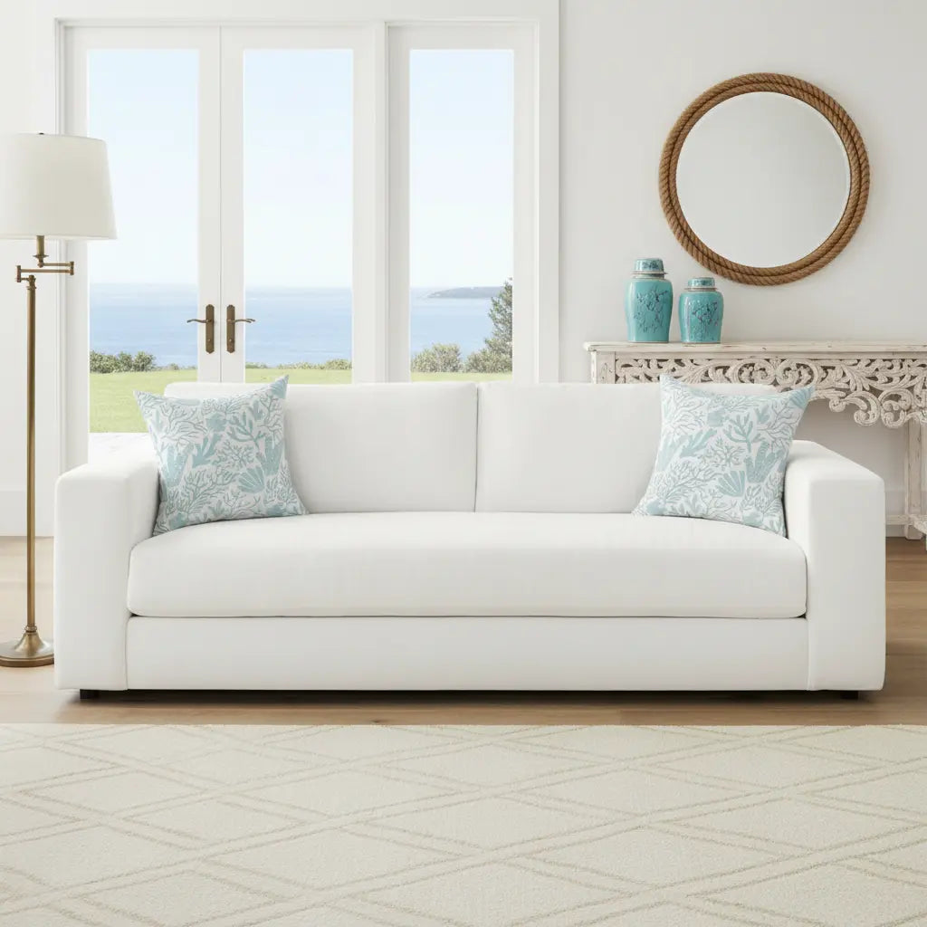 Coral Gardens Throw Pillow in aqua coastal reef pattern on white sofa with ocean view.