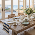 Navy and ivory striped table runner with natural rope trim and decorative loop tassels draped over a wood dining table.